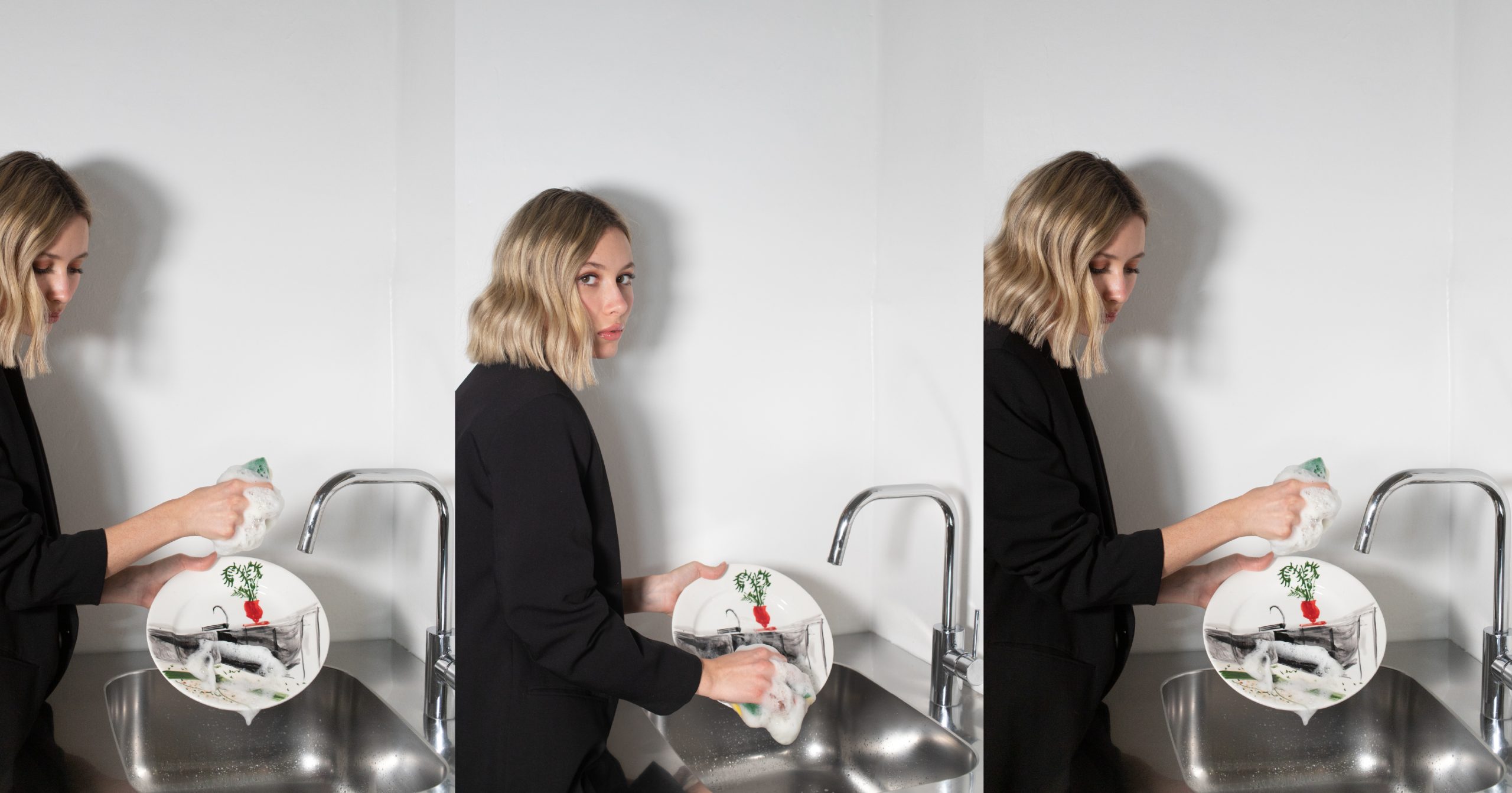 Donna con abbigliamento nero lava a mano un piatto illustrato in un lavello minimal, in un ambiente luminoso e contemporaneo