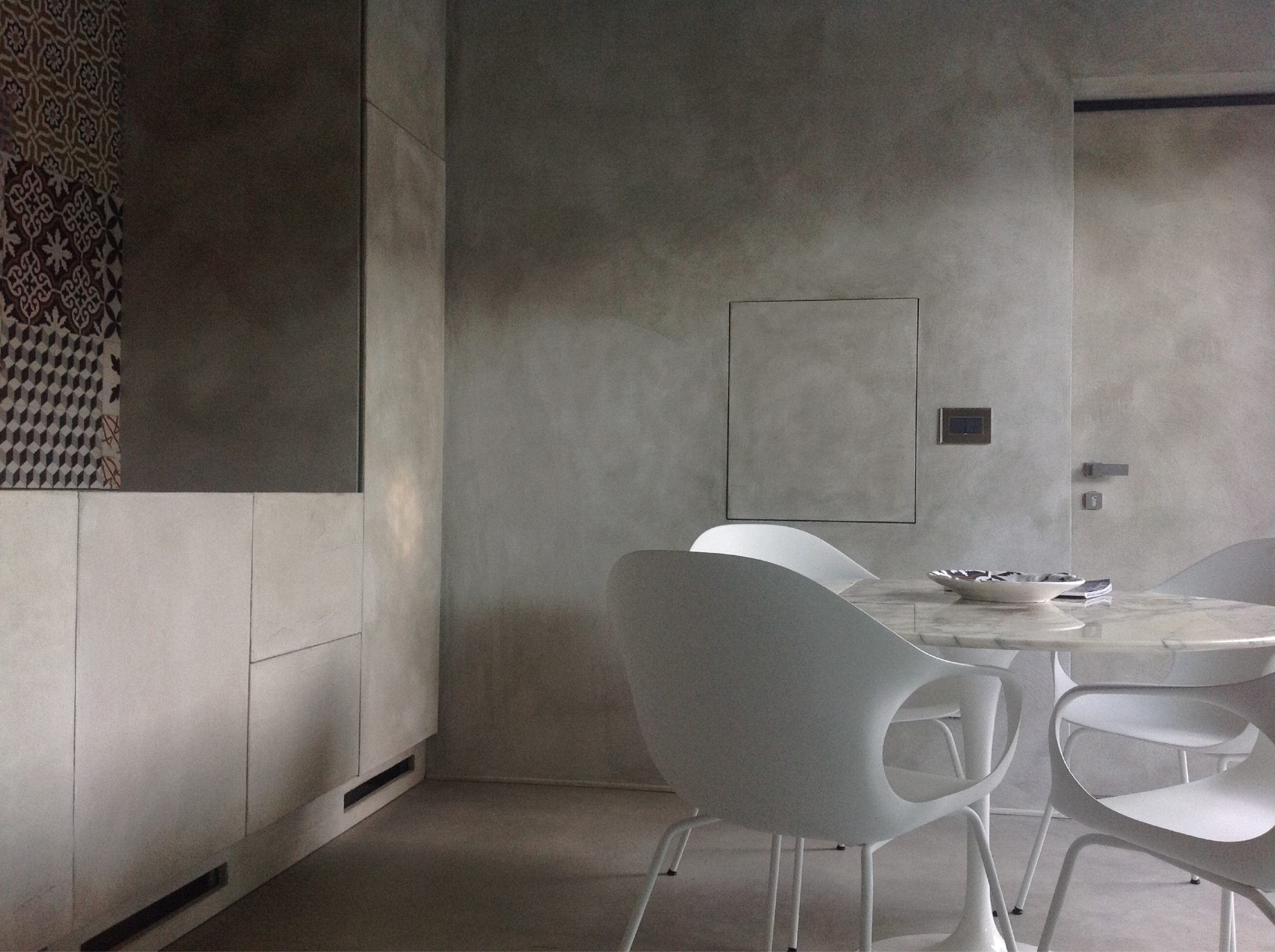 Interno del bastidon con zona pranzo, pareti grigie materiche, tavolo in marmo e sedie bianche dal design contemporaneo.