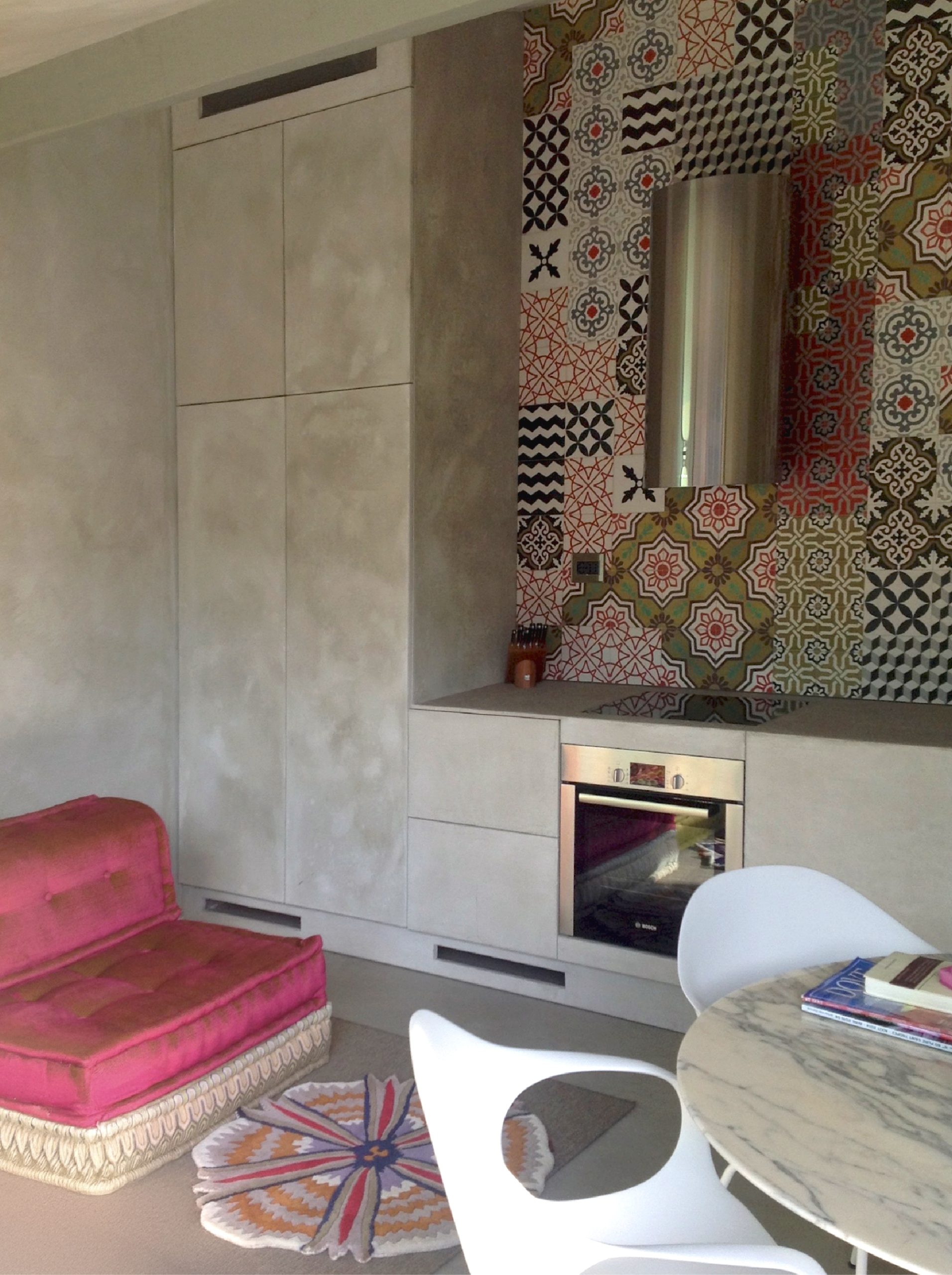 Interno del bastidon con cucina decorata da piastrelle grafiche, armadi grigi, seduta fucsia e tavolo in marmo con sedie bianche.