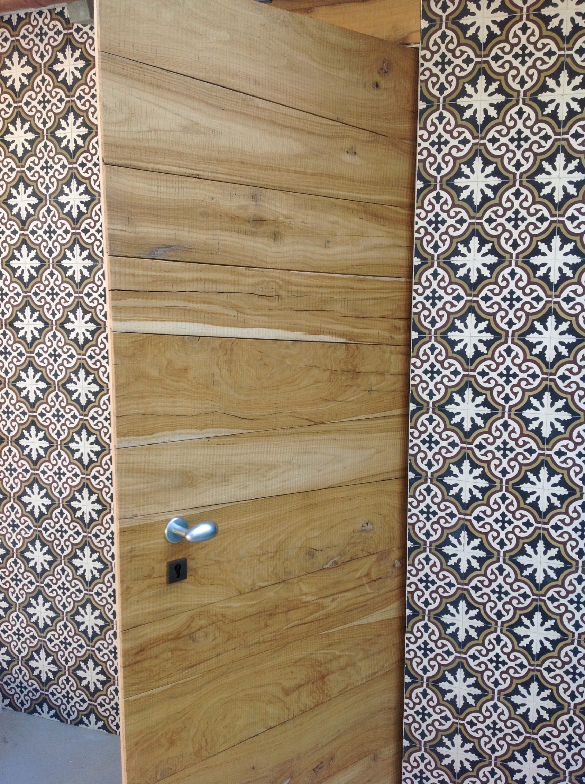 Dettaglio di porta in legno naturale incorniciata da piastrelle decorative grafiche nei toni del nero, bianco e marrone.