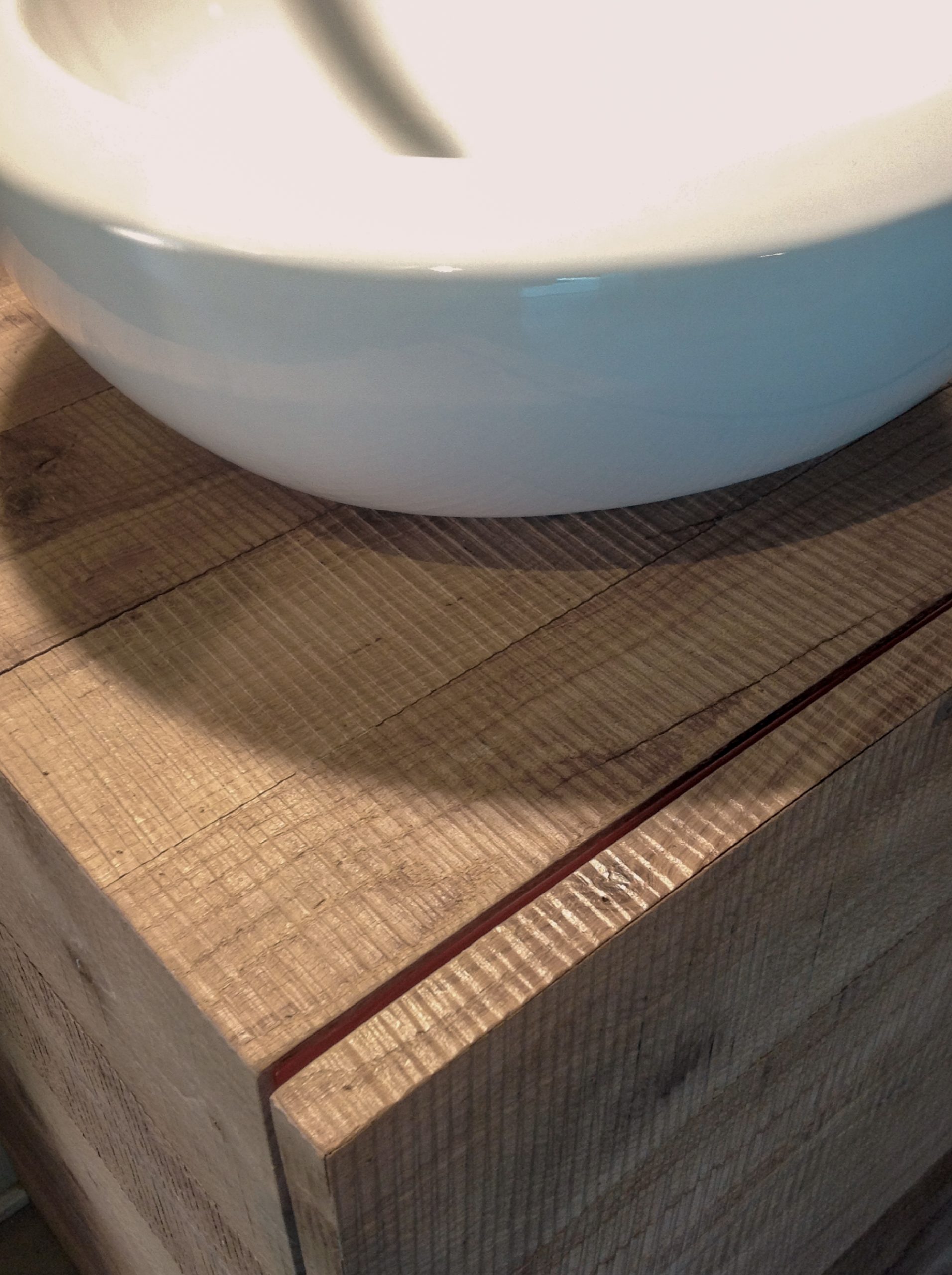 Dettaglio del lavabo bianco appoggiato su mobile bagno in legno naturale con venature marcate e taglio minimale.