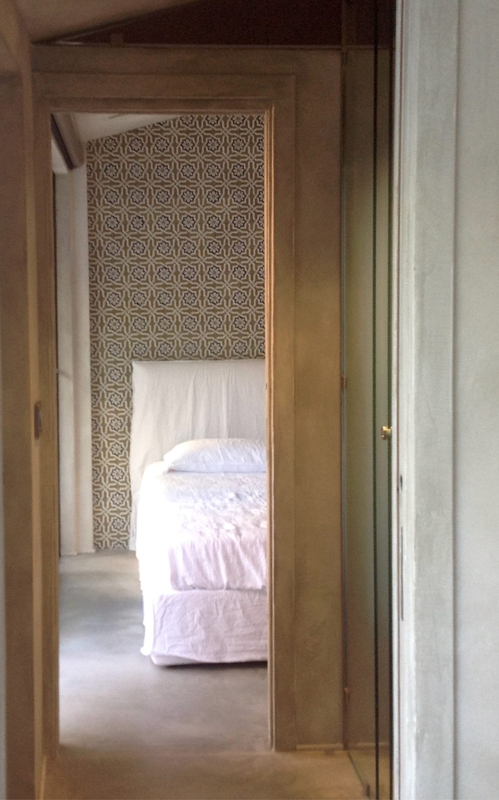 Vista dalla zona di passaggio verso la camera da letto, con parete decorata da piastrelle grafiche e letto bianco sul fondo.