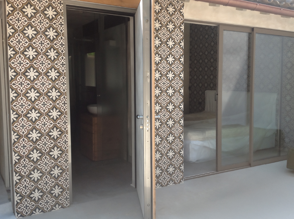 Facciata esterna con camera da letto visibile attraverso la vetrata e pareti rivestite da piastrelle decorative a motivo grafico