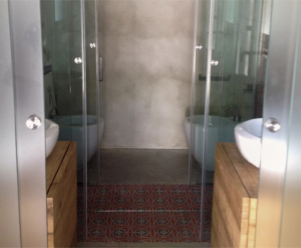 Bagno del bastidon con parete grigia materica, docce in vetro, pavimento decorato e mobili lavabo in legno
