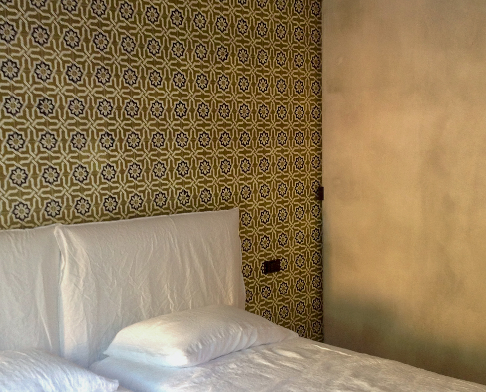 Camera da letto del progetto A Bastidon in Saint-Tropez con testiera bianca, parete decorata da piastrelle grafiche e finitura grigia materica